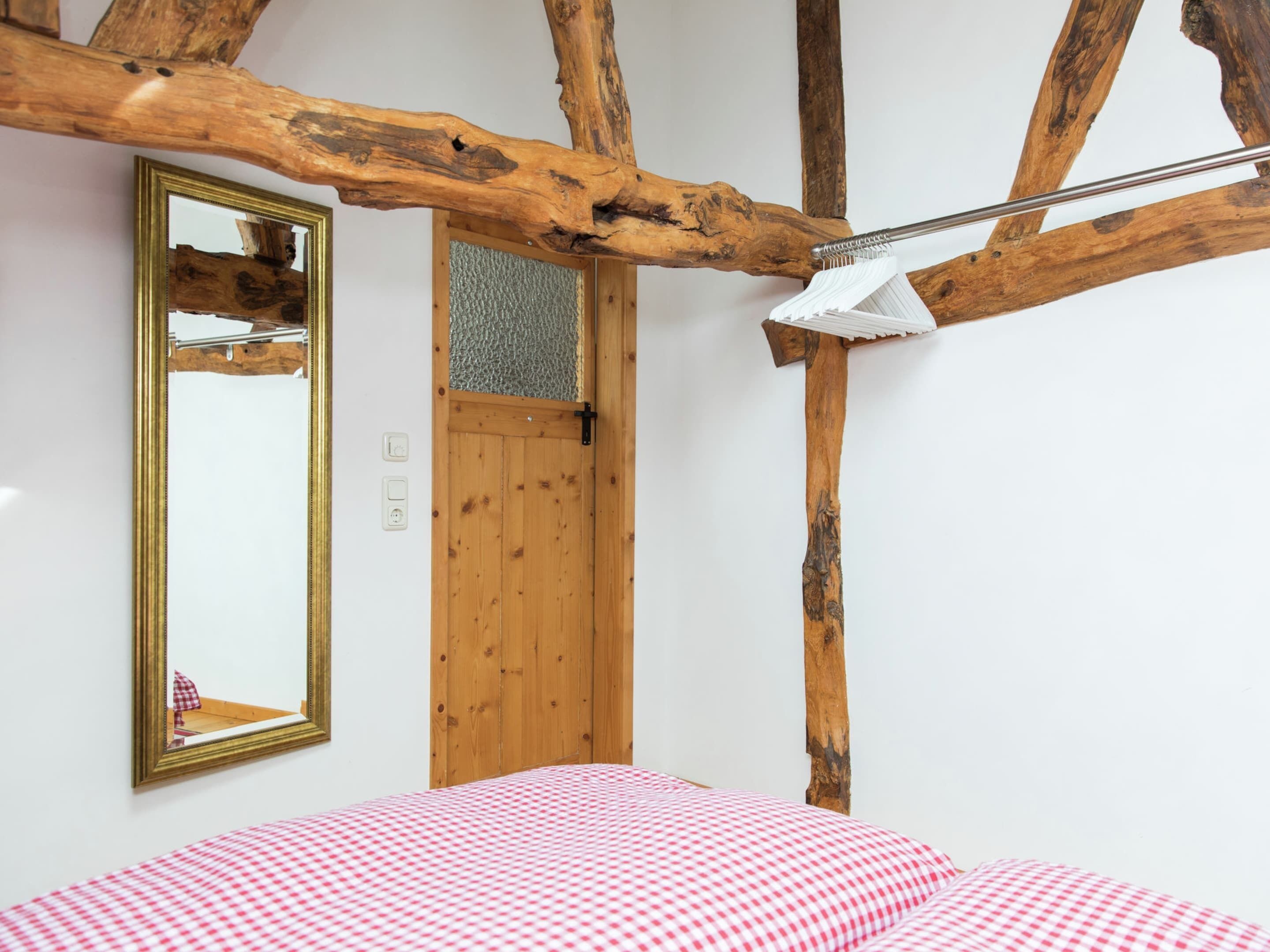 A bedroom with a wooden ceiling, a bed with a checkered bedspread, a mirror, and a door.
