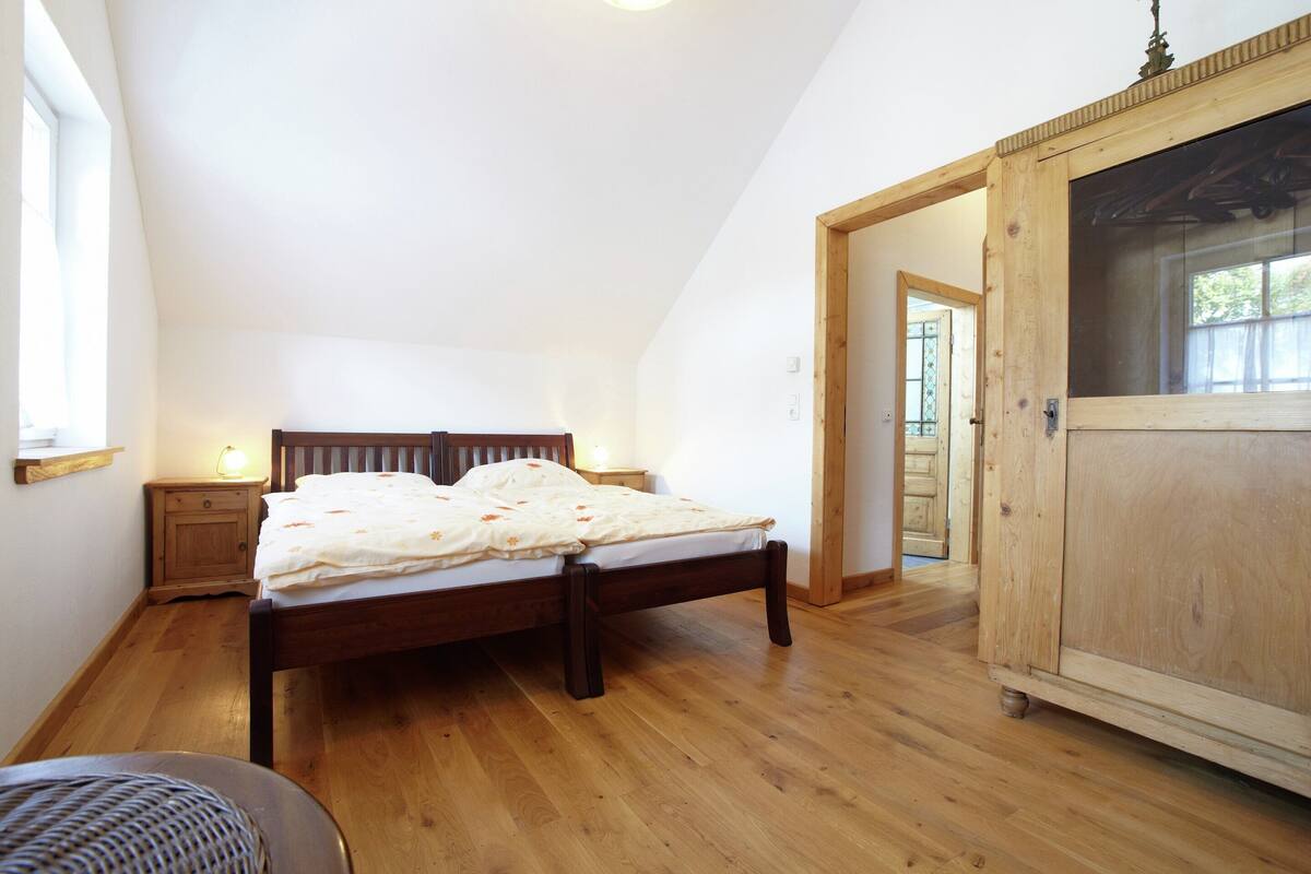 A bedroom with a wooden bed, a nightstand with a lamp, and a large wooden cabinet.