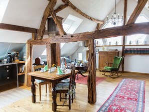 A loft-style room with exposed wooden beams, a dining table with chairs, a rocking chair, a chandelier, and a red patterned rug. - Modernes Apartment mit Parkplatz in der Eifel (Schleiden)