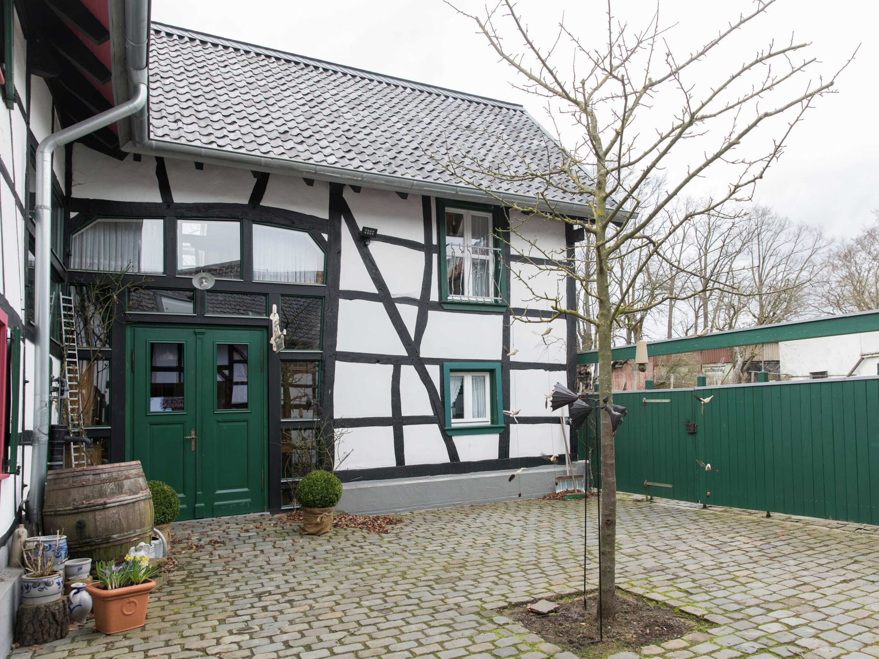 Ein traditionelles Fachwerkhäuschen mit grüner Tür, ein kleiner Garten mit Blumentöpfen und ein Pflasterhof.