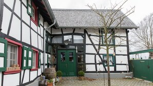 A traditional half-timbered building with a green door, potted plants, and a cobblestone courtyard.