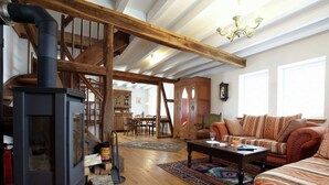 A cozy living room with a wood-burning stove, a staircase, a dining area, and a sofa.