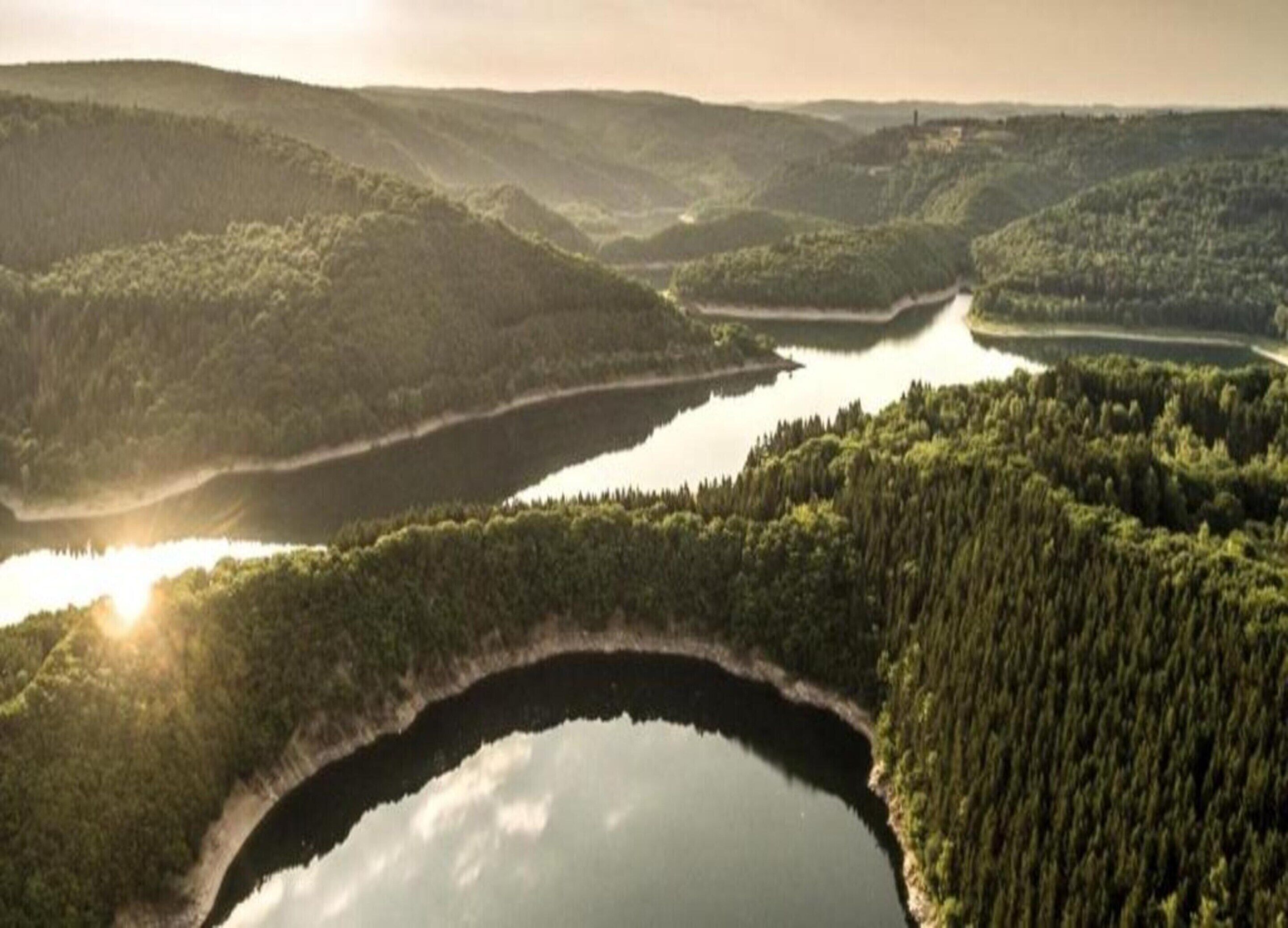 A natural landscape with a lake surrounded by dense forest and hills.