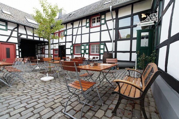 A traditional European building with a sign indicating a restaurant. There are outdoor tables and chairs arranged on a cobblestone patio. - Modernes Apartment mit Parkplatz in der Eifel (Schleiden)