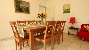 A dining room with a wooden table and chairs, a vase of sunflowers, and a red sofa. - Lovely Farmhouse in Wijlre With Forest Nearby (Wijlre)