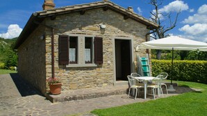 A stone cottage with a patio, a table with chairs, and a white umbrella. - Beautiful Apartment With Panoramic Swimming Pool (Città di Castello)