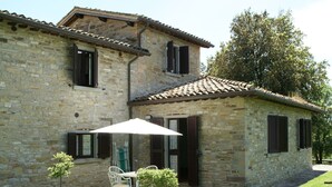 A stone building with a tiled roof, a patio with a table and chairs, and a small tree. - Beautiful Apartment With Panoramic Swimming Pool (Città di Castello)