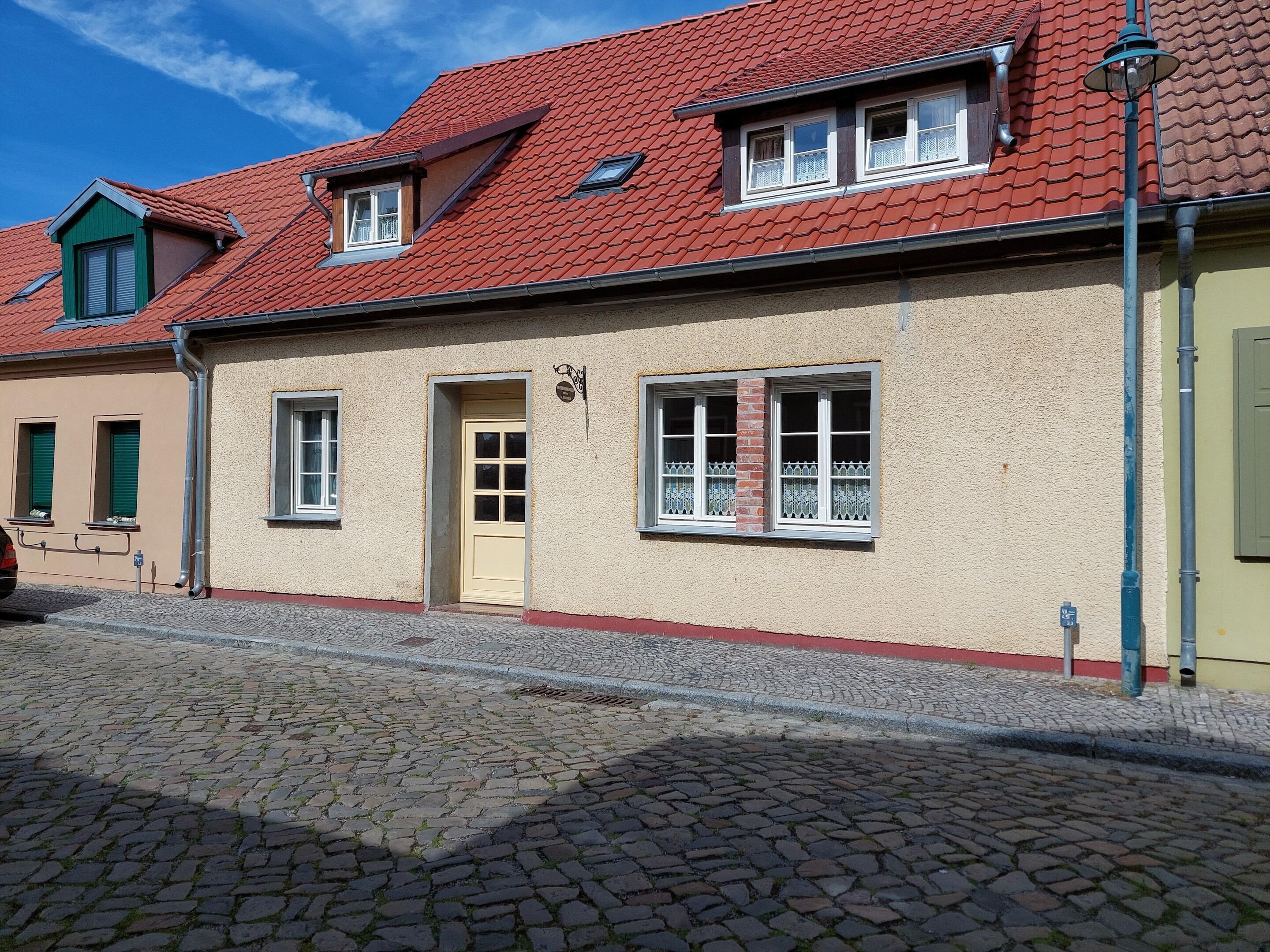 A building with a red-tiled roof, a yellow door, and multiple windows with white frames.