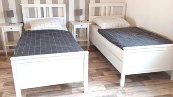A bedroom with two single beds, a nightstand with a lamp, and a small drawer unit.
