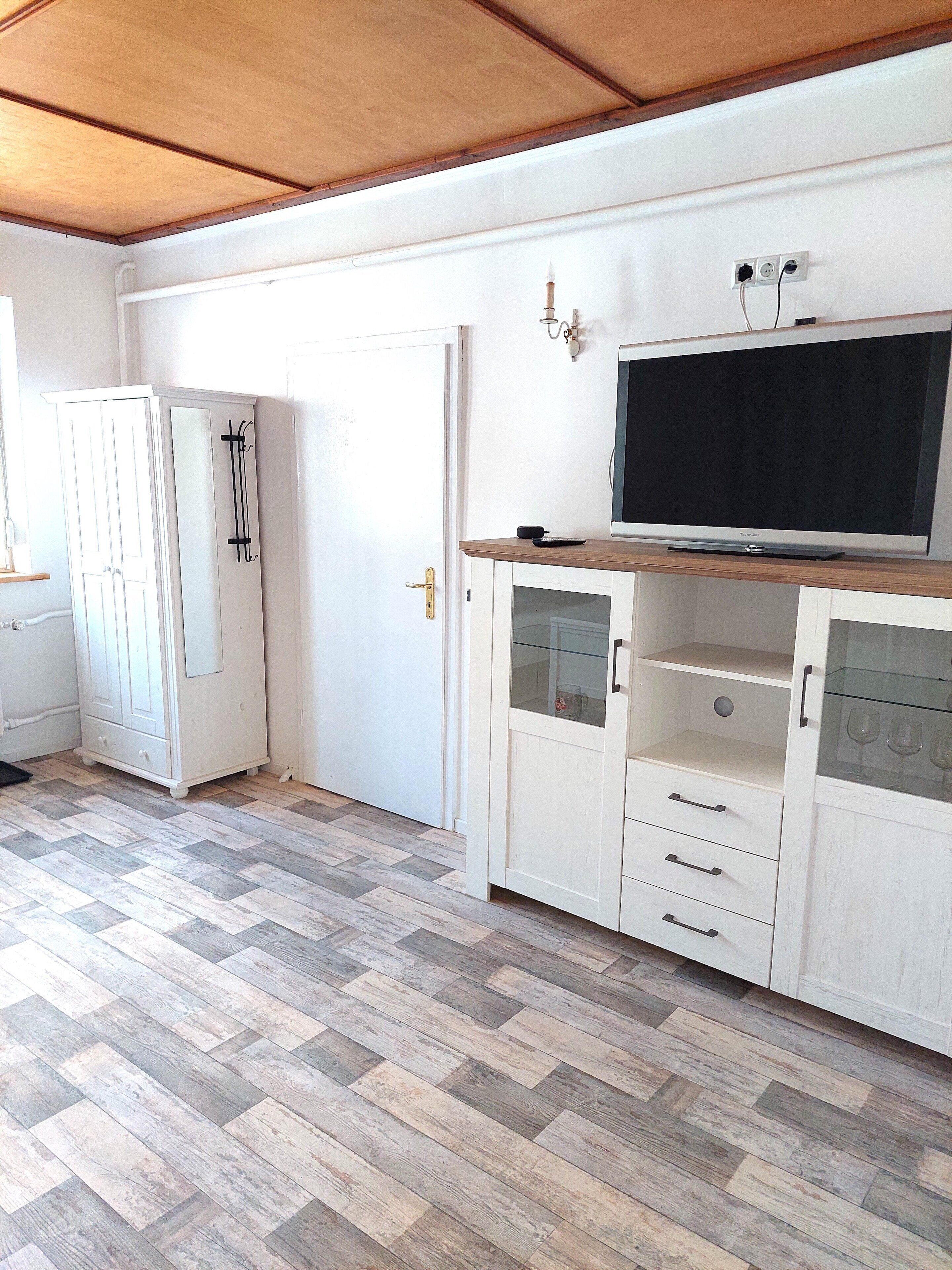 Ein Zimmer mit einem großen Flachbildfernseher auf einer Holzkommode, einem weißen Kleiderschrank und einem Holzboden mit Fischgrätmuster.
