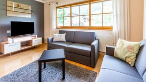 A modern living room with a flat-screen TV, grey sofas, a coffee table, and a large window with curtains. - Quietly-located Apartment Near the Center of Radstadt (Radstadt)