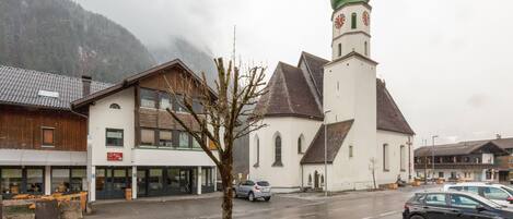 Una iglesia con una cúpula verde y una torre del reloj, un edificio con un letrero, y un árbol en primer plano.