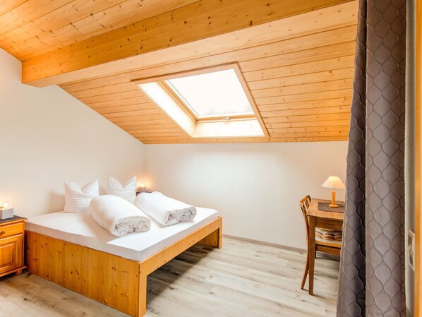 Un dormitorio con tragaluz, cama de madera, mesitas de noche y una silla.