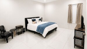 A modern hotel room with a large bed, a desk, a chair, a small table, a ceiling fan, and a window with curtains. - 2BD-RemoteWork-Extd Stay Discounts-PetsOK-Central (Corpus Christi)