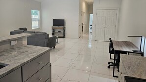 A spacious living area with a large window, a flat-screen TV, a dining table, and a kitchen counter. - 2BD-RemoteWork-Extd Stay Discounts-PetsOK-Central (Corpus Christi)