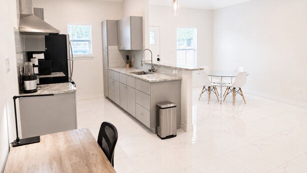 A modern kitchen with a central island, a dining area with a table and chairs, and a view of the city through large windows. - 2BD-RemoteWork-Extd Stay Discounts-PetsOK-Central (Corpus Christi)