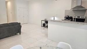 A modern kitchen with a central island, a dining area with a glass table, and a grey sofa. - 2BD-RemoteWork-Extd Stay Discounts-PetsOK-Central (Corpus Christi)