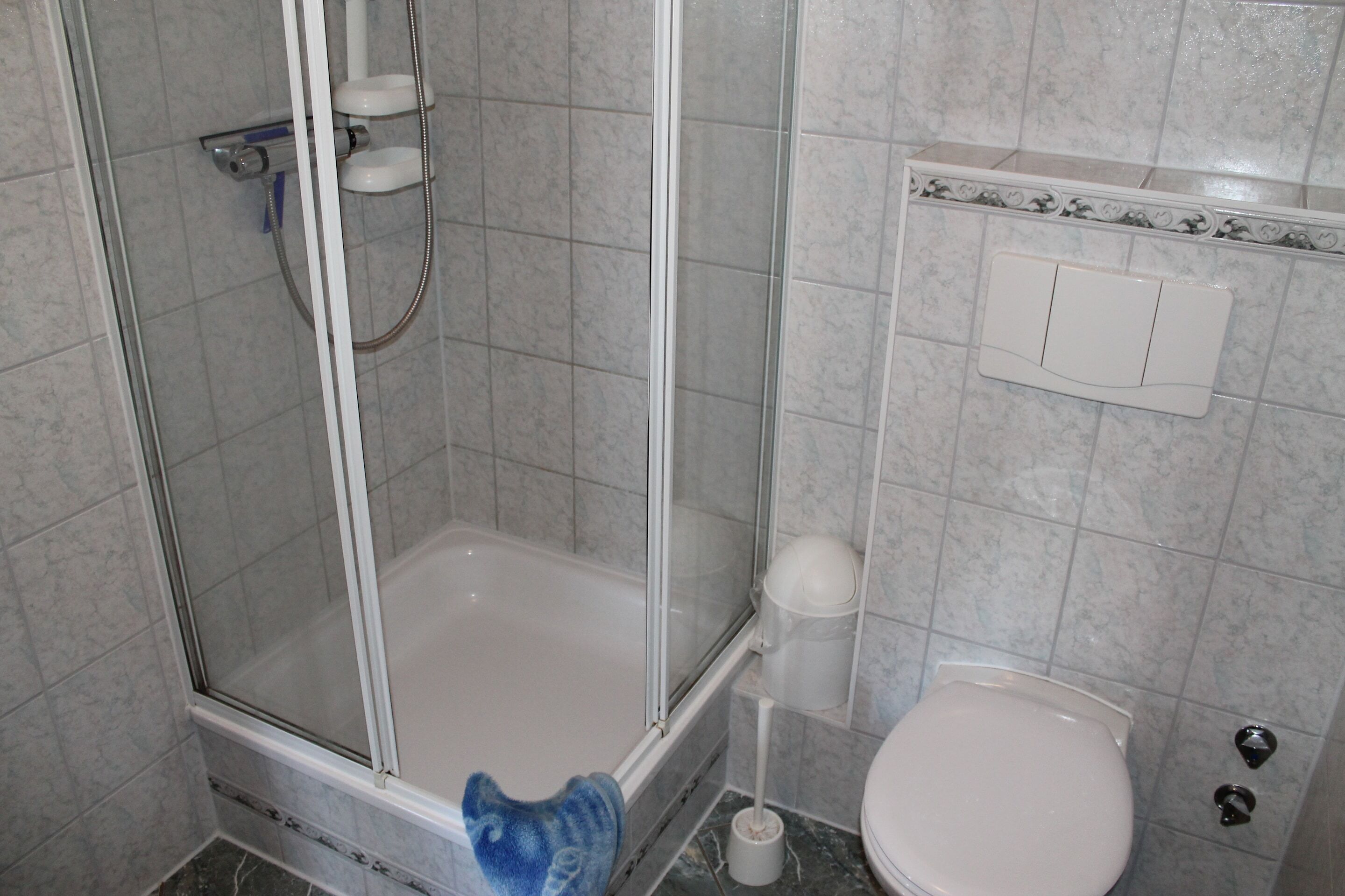 A bathroom with a glass-enclosed shower, a white bathtub, a toilet, and a wall-mounted toilet paper holder.