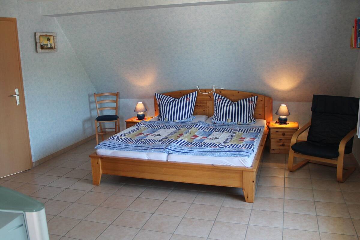 A bedroom with a wooden bed, two bedside tables with lamps, a chair, and a door.
