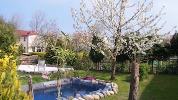 A garden with a swimming pool, surrounded by trees and a house in the background.