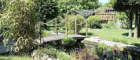 A garden with a small pond, a wooden bridge, and a rope barrier.