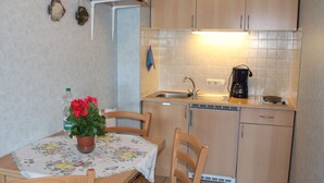 Une cuisine compacte avec des meubles en bois, un évier et une machine à café. On y trouve une table avec des chaises et une plante en pot.