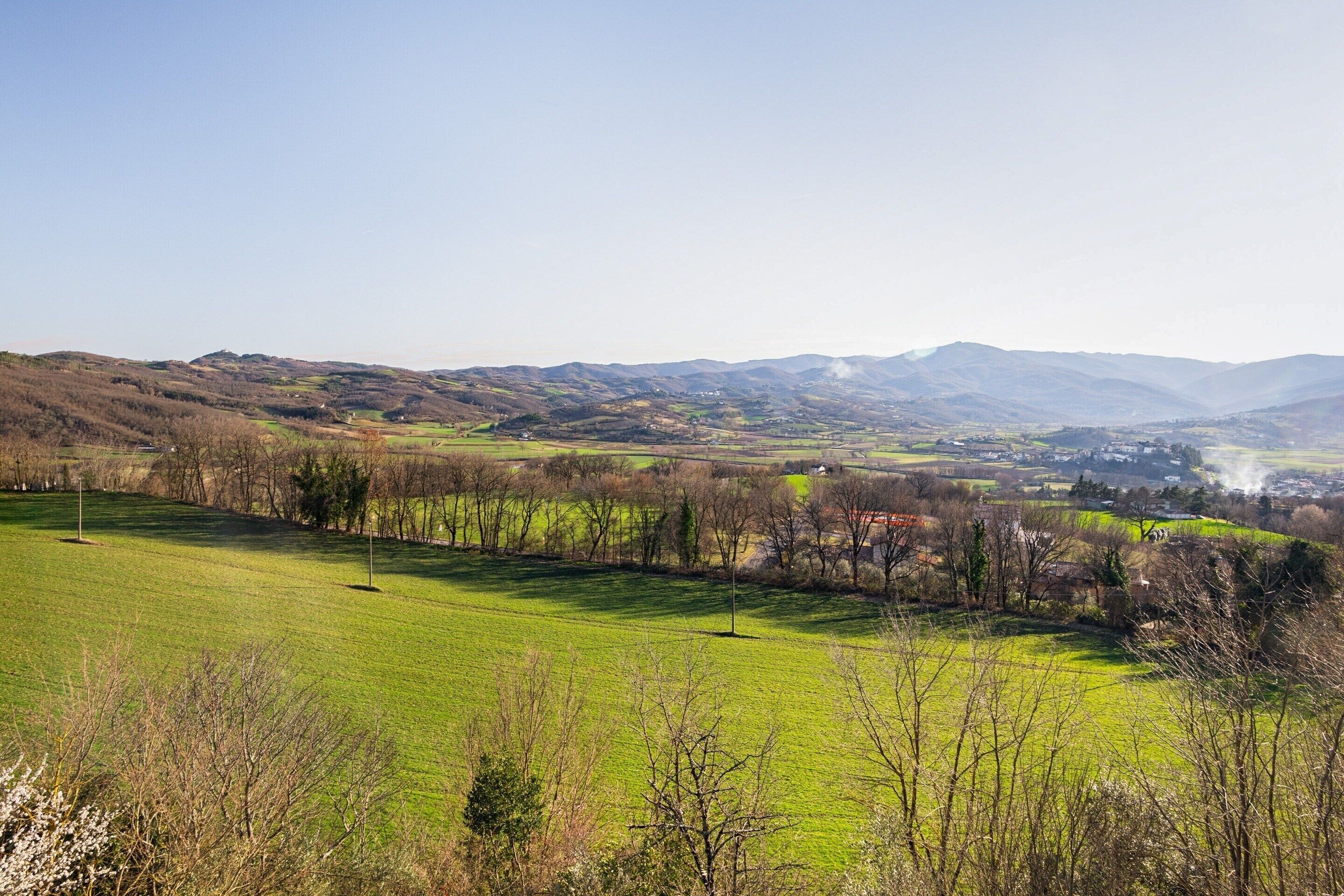 A panoramic view of a rural landscape with rolling hills, a green field, and a distant village.