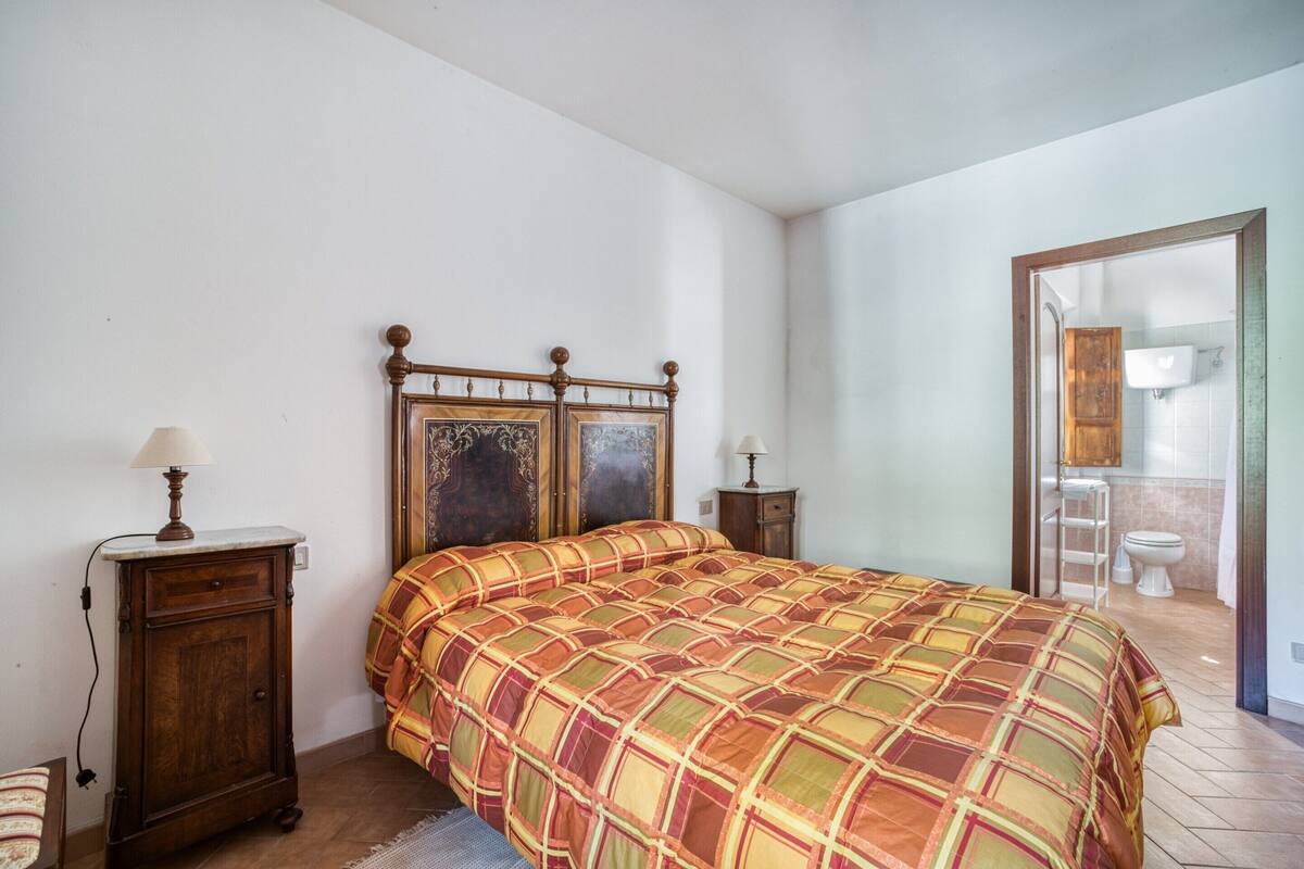 A bedroom with a bed, a nightstand, a lamp, and a bathroom visible through an open door.