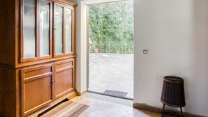 Un meuble en bois avec des portes en verre, un petit tabouret et une vue sur un balcon doté d’une balustrade et bordé d’arbres.