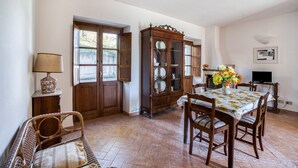 Un coin repas avec une table dressée pour quatre personnes, entourée de chaises en bois, d’un meuble avec des portes en verre et d’une lampe posée sur une table d’appoint.