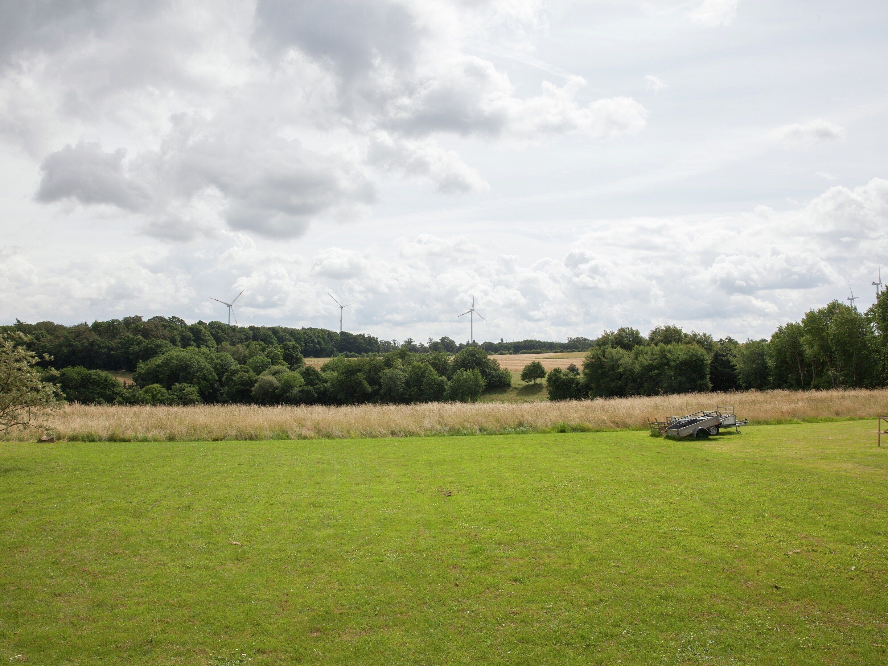 A grassy field with wind turbines in the background and a trailer in the foreground.