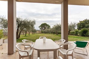 A covered outdoor area with a table and chairs, overlooking a grassy landscape with trees. - Cozy Apartment With Swimming Pool and gym on Lake Trasimeno (Tuoro sul Trasimeno)