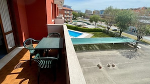 A balcony with a table and chairs, overlooking a swimming pool and a green lawn. - Lovely Holiday Home in Porto Santa Margherita With Pool (Caorle)