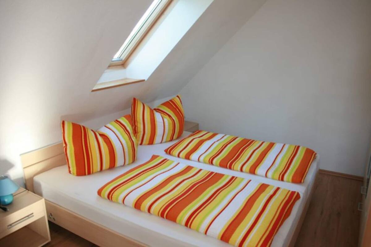 A small, single-bed room with a skylight, striped bedding, and a bedside table with a lamp.