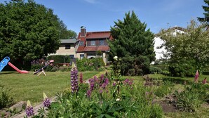 A residential garden with a playground, a house with a red roof, and various flowering plants. - Beautiful Apartment in Robertsdorf With Garden (Blowatz)