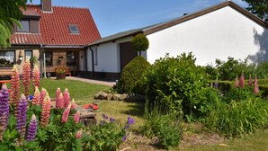 A house with a red roof, white exterior walls, and a garden with various flowers. - Beautiful Apartment in Robertsdorf With Garden (Blowatz)