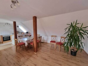 A dining area with a wooden table and chairs, a potted plant, and a kitchen in the background. - Beautiful Apartment in Robertsdorf With Garden (Blowatz)