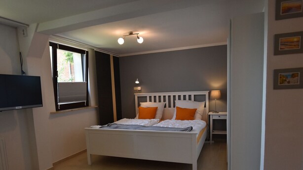 A bedroom with a bed, bedside table, lamp, and a TV on the wall. - Beautiful Apartment in Robertsdorf With Garden (Blowatz)