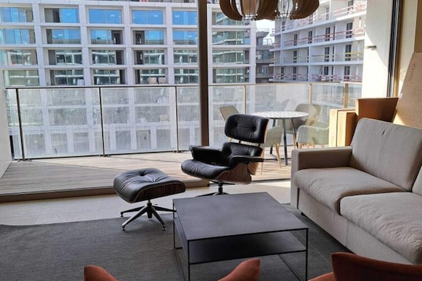 En moderne stue med sofa, læderstol, lille bord og glasvæg.