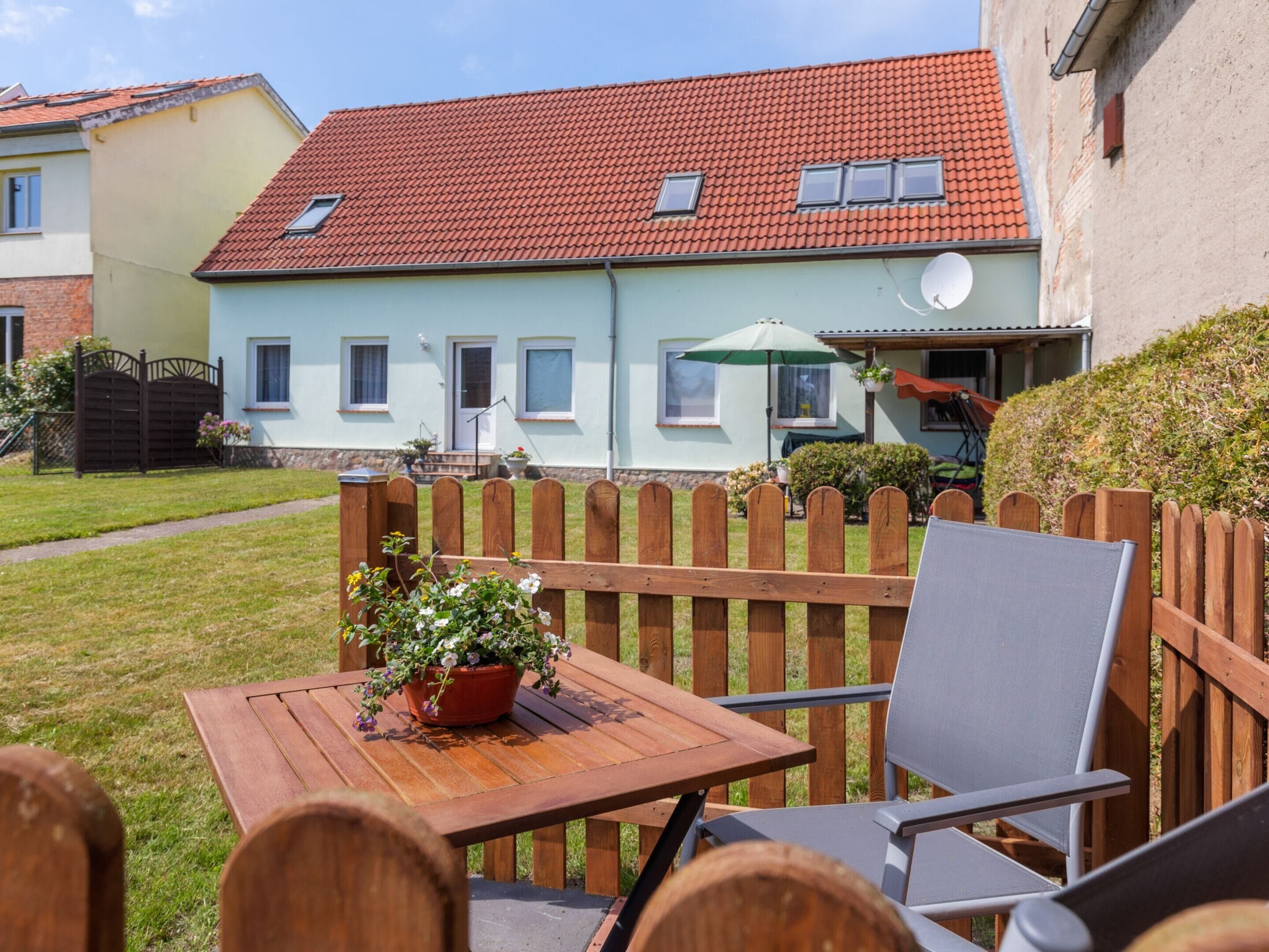 A wooden table with a potted plant, a chair, and a view of a house with a red-tiled roof and a satellite dish.