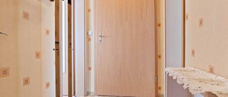 A hallway with a wooden door, a coat rack, and a small table with a lace tablecloth.