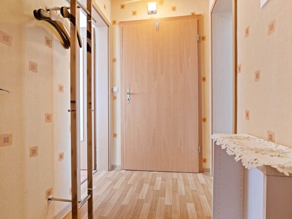 Un couloir avec une porte en bois, un porte-manteau et une petite table recouverte d’une nappe en dentelle.
