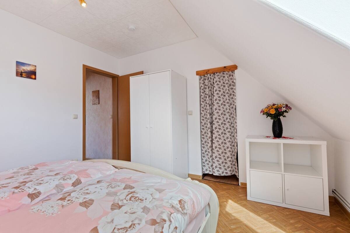 A bedroom with a bed, a wardrobe, a small cabinet, and a window with curtains.