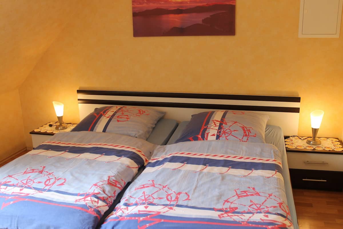 A bed with a striped bedspread and matching pillows, two bedside tables with lamps, and a painting on the wall.