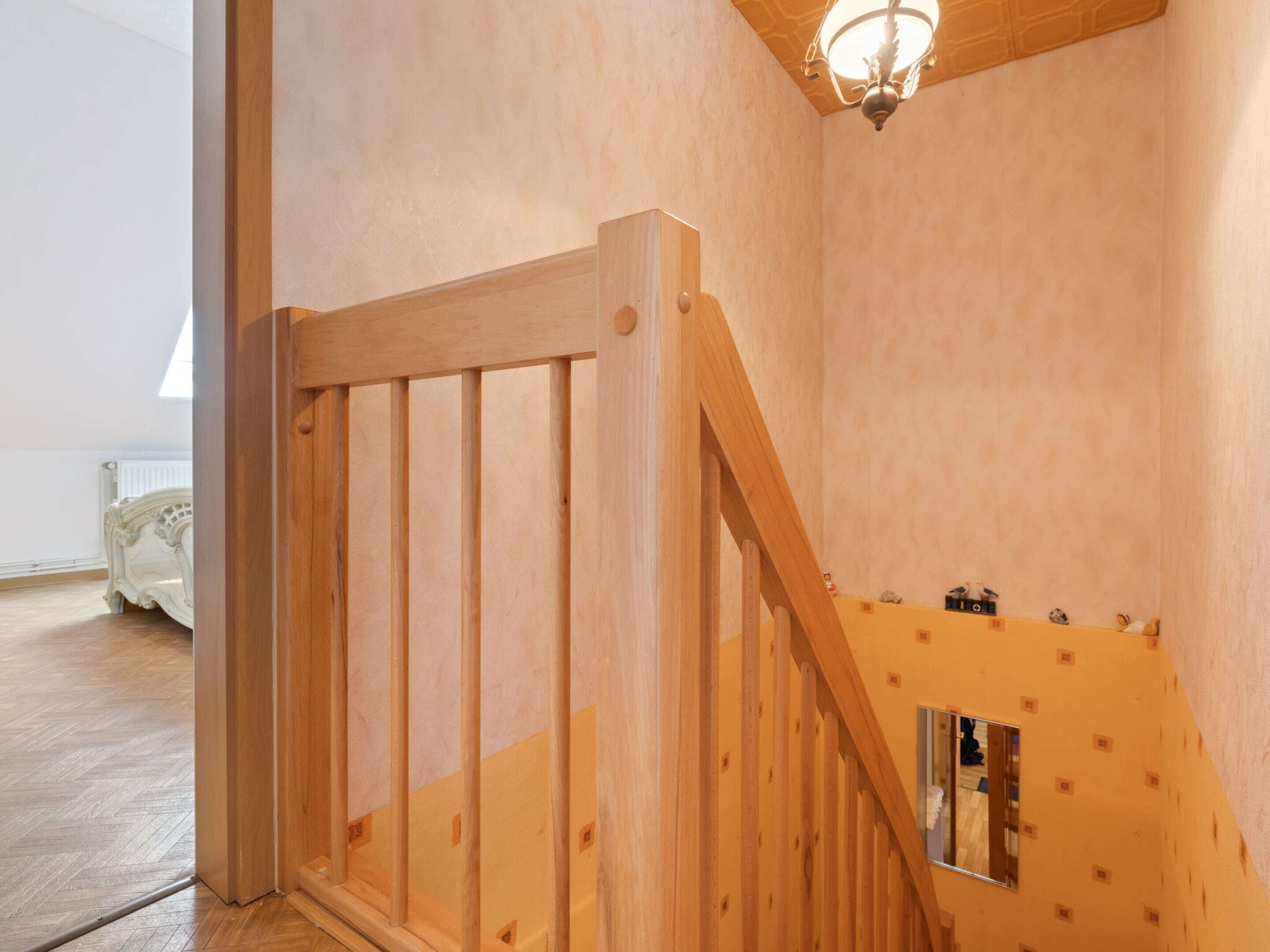 Eine Holztreppe mit Handlauf, eine Leuchte darüber und ein weißer Heizkörper im Hintergrund.