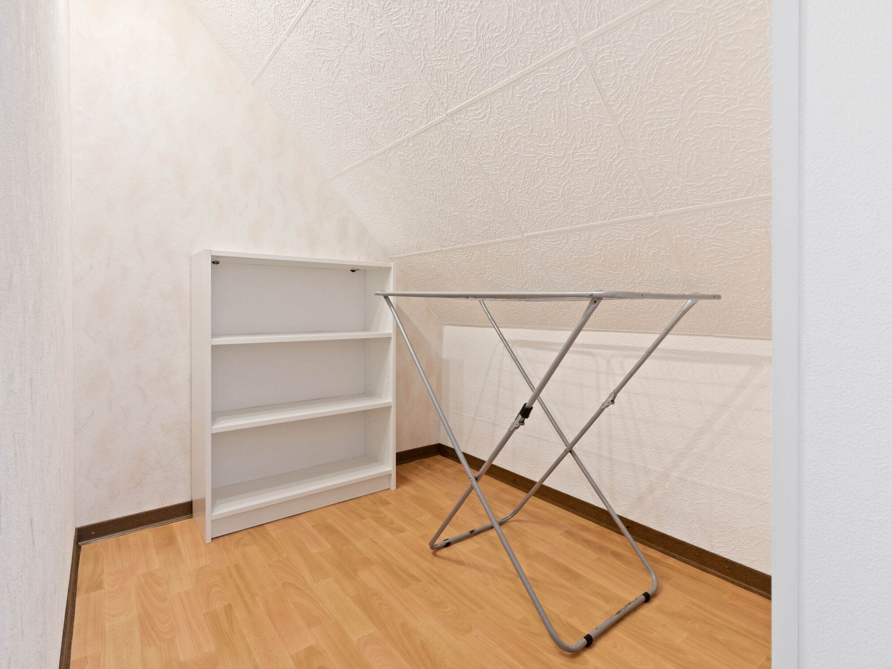 A corner room with a metal drying rack and a white shelving unit against a textured wall.