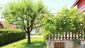 A residential area with a large tree, a small brick structure with a wooden gate, and a well-maintained lawn. - Modern Apartment With Garden Near the Petzen ski Area in Eberndorf / Carinthia (Eberndorf)
