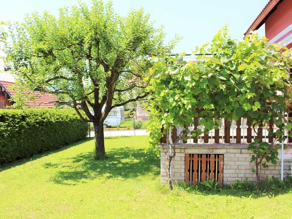 Un quartier résidentiel avec un grand arbre, une petite construction en briques dotée d’un portail en bois et une pelouse bien entretenue.