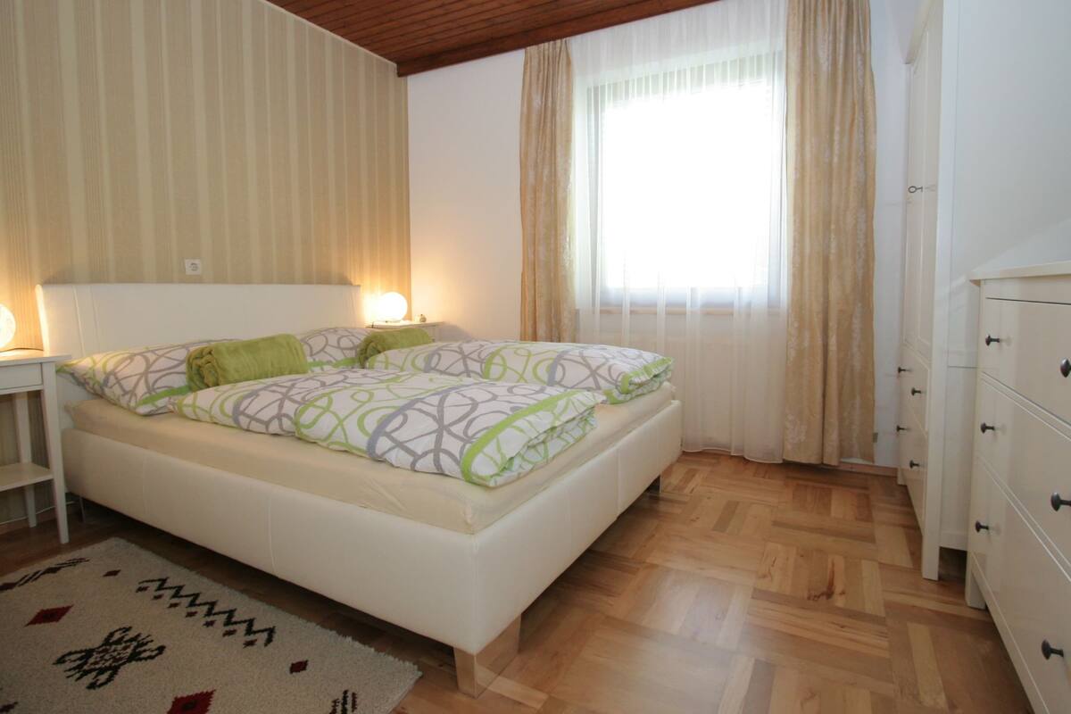 A bedroom with a bed, bedside tables, a dresser, and a window with curtains.