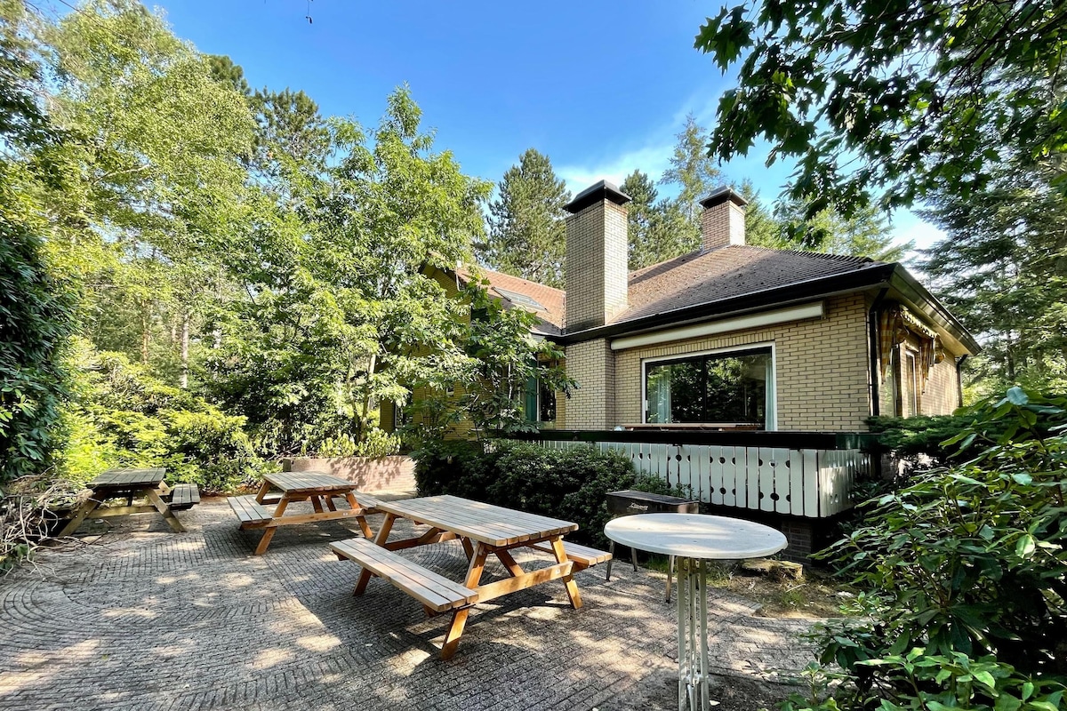 A rustic cabin with a brick exterior, surrounded by dense greenery and a wooden deck.